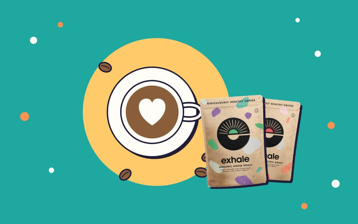 A cup of coffee with a heart in the foam next to two bags of Exhale organic coffee