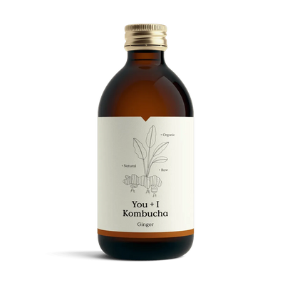 You + I Ginger raw kombucha in an amber glass bottle with a gold cap and a cream label with a botanical line drawing and an orange band.