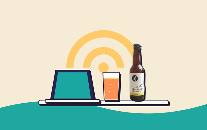 A laptop on a table with a glass of kombucha and a Wi-Fi symbol