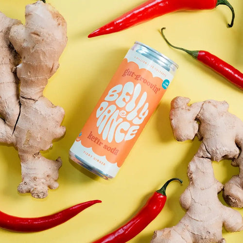 A can of Belly Dance Fiery Ginger water kefir lying on a yellow background with fresh ginger root and red chillies.