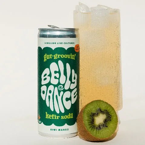 A can of Belly Dance Kiwi Mango water kefir beside a tall glass of ice and half a kiwi.