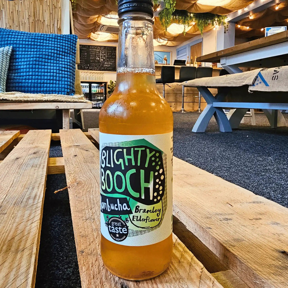A bottle of Blighty Booch Bramley Apple & Elderflower raw kombucha on a wooden pallet table in the Otley taproom.