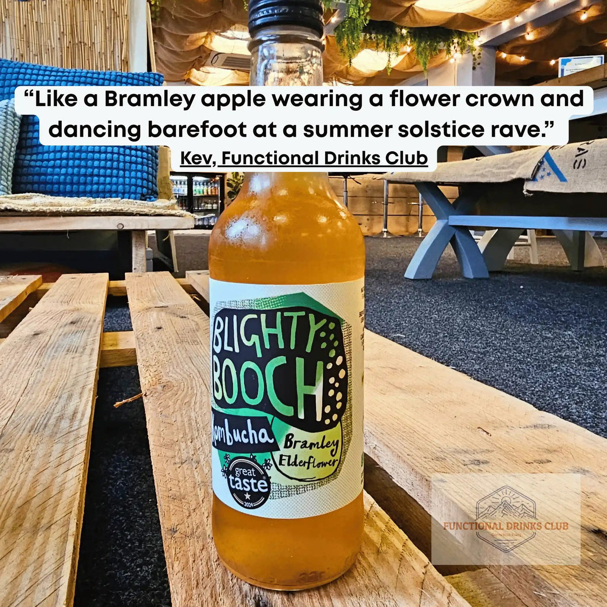 Blighty Booch Bramley Apple & Elderflower raw kombucha on a wooden pallet table in the Otley taproom, with Kev's tasting note: "Like a Bramley apple wearing a flower crown and dancing barefoot at a summer solstice rave."