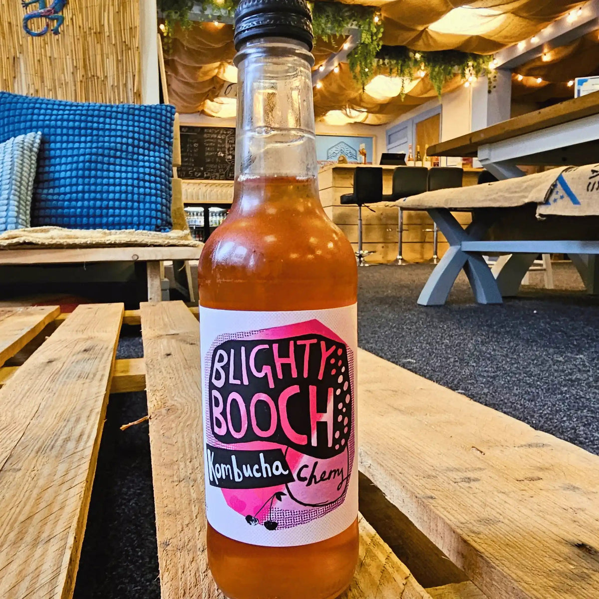 A bottle of Blighty Booch Cherry raw kombucha on a wooden pallet table in the Otley taproom.