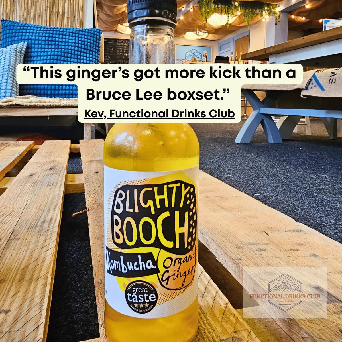 Blighty Booch Organic Ginger raw kombucha on a wooden pallet table in the Otley taproom, with Kev's tasting note: "This ginger's got more kick than a Bruce Lee boxset."