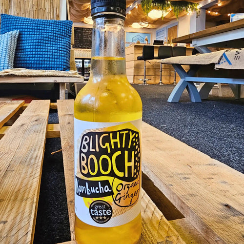 A bottle of Blighty Booch Organic Ginger raw kombucha on a wooden pallet table in the Otley taproom.