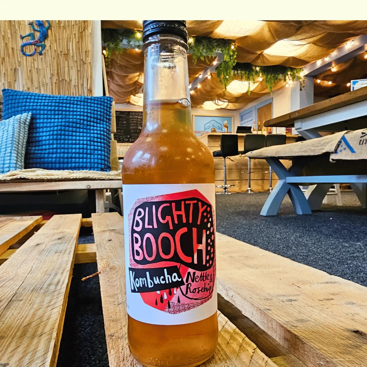A bottle of Blighty Booch Nettle & Rosehip raw kombucha on a wooden pallet table in the Otley taproom.