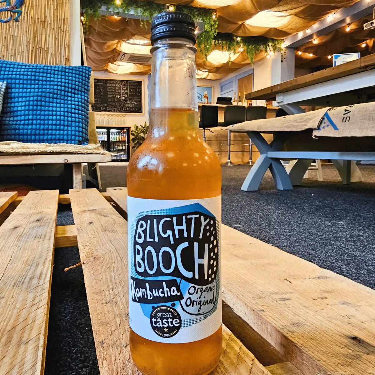 A bottle of Blighty Booch Organic Original raw kombucha on a wooden pallet table in the Otley taproom.