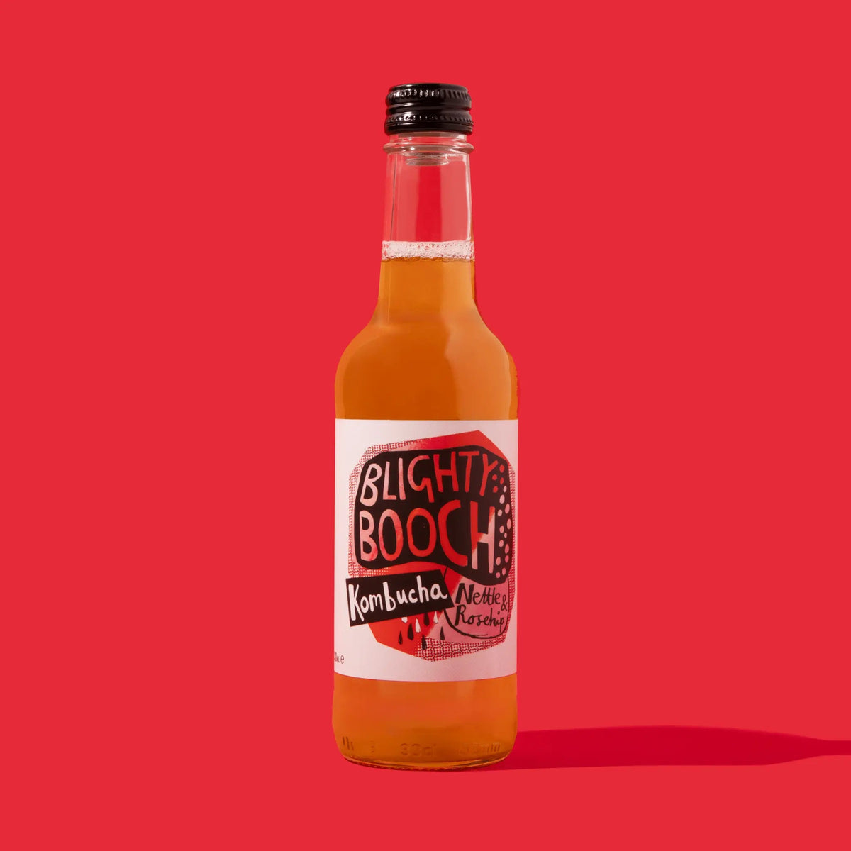 Bottle of Blighty Booch Nettle & Rosehip Kombucha on a red background