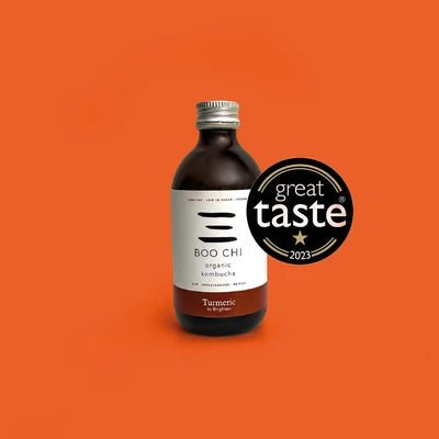 A bottle of Boo Chi Turmeric & Black Pepper raw kombucha on a bright orange background with its Great Taste 2023 award badge.