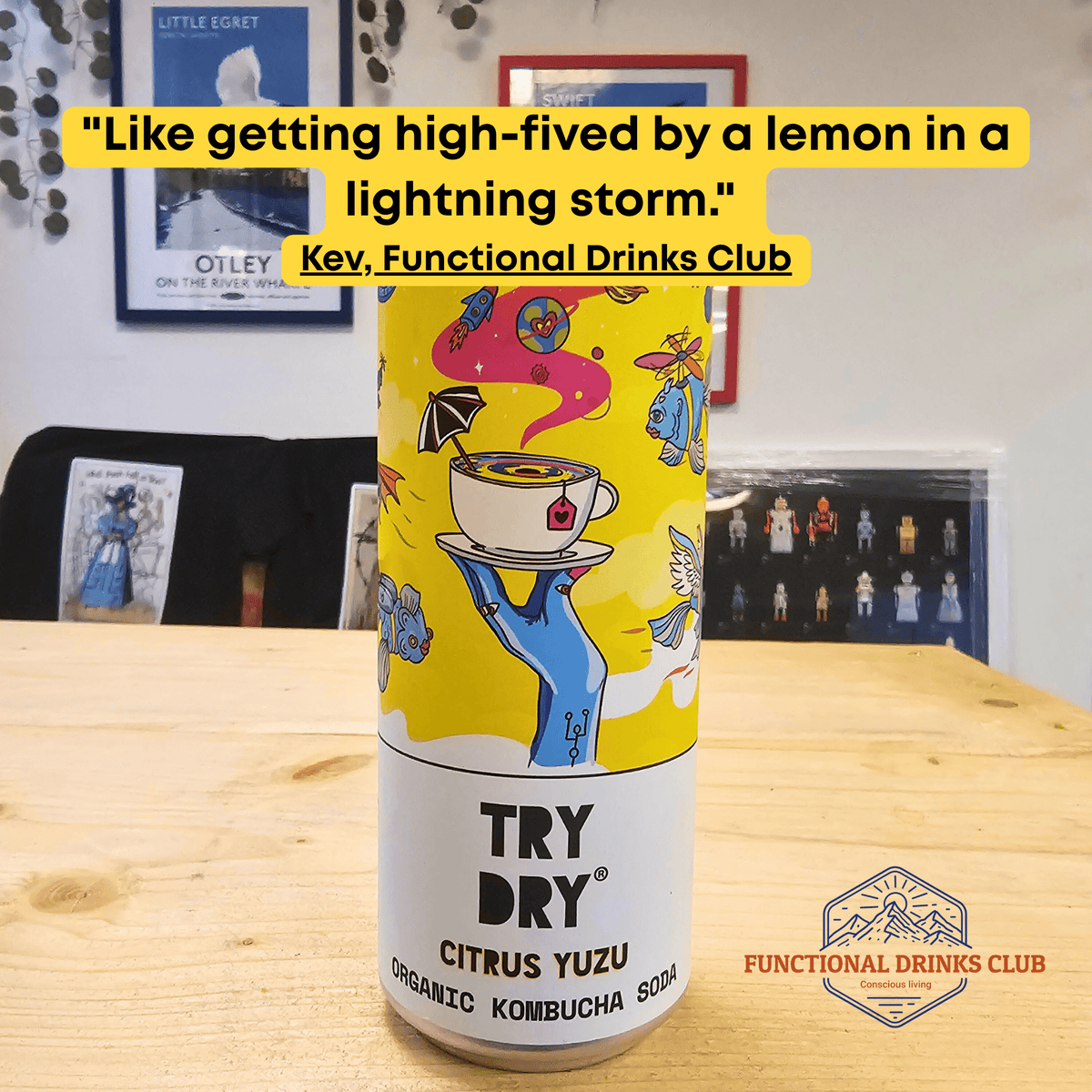 A can of Counter Culture Citrus Yuzu raw kombucha on a wooden table in front of framed Otley art prints, with Kev's tasting note: "Like getting high-fived by a lemon in a lightning storm."
