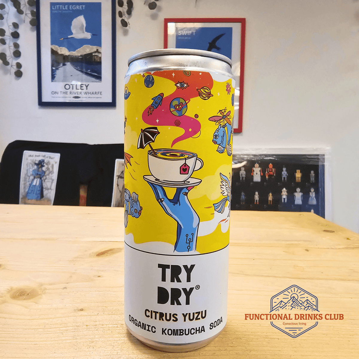 A can of Counter Culture Citrus Yuzu raw kombucha on a wooden table in front of framed Otley art prints.