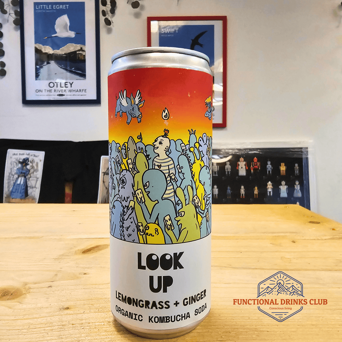 A can of Counter Culture Lemongrass & Ginger raw kombucha on a wooden table in front of framed Otley art prints.