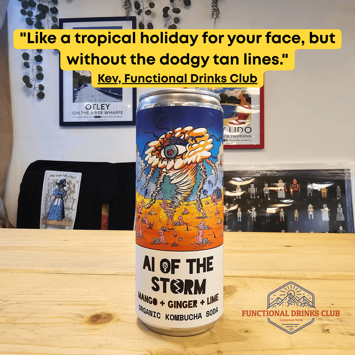 A can of Counter Culture Mango, Ginger & Lime raw kombucha on a wooden table in front of framed Otley art prints, with Kev's tasting note: "Like a tropical holiday for your face, but without the dodgy tan lines."