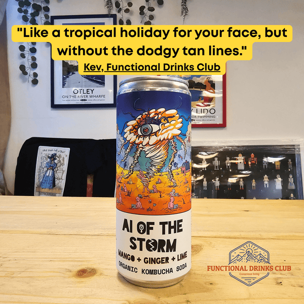 A can of Counter Culture Mango, Ginger & Lime raw kombucha on a wooden table in front of framed Otley art prints, with Kev's tasting note: "Like a tropical holiday for your face, but without the dodgy tan lines."