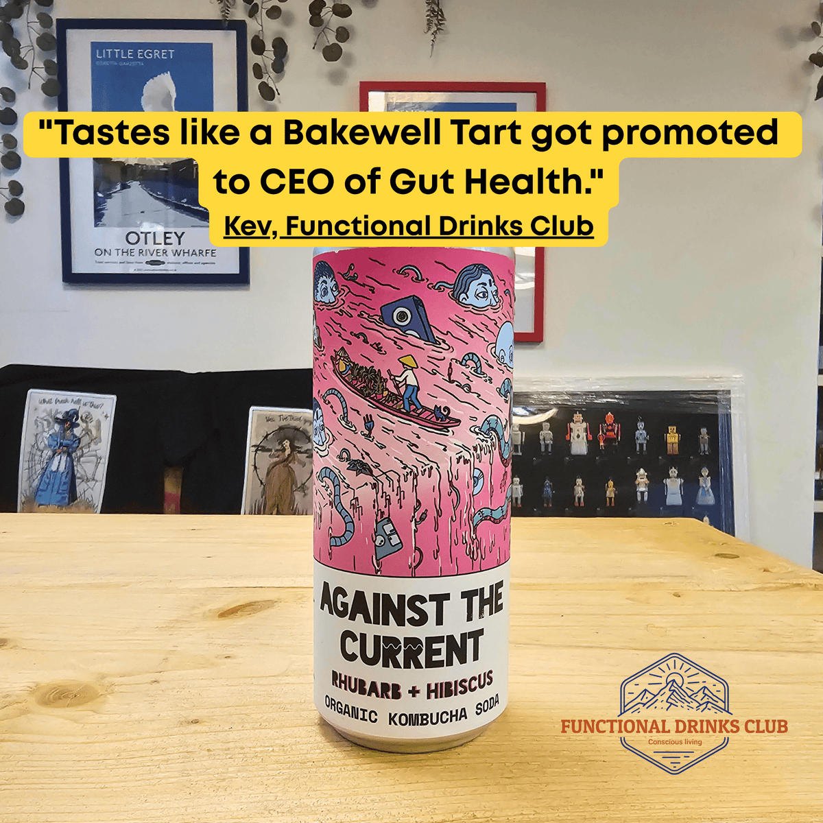 A can of Counter Culture Rhubarb & Hibiscus raw kombucha on a wooden table in front of framed Otley art prints, with Kev's tasting note.
