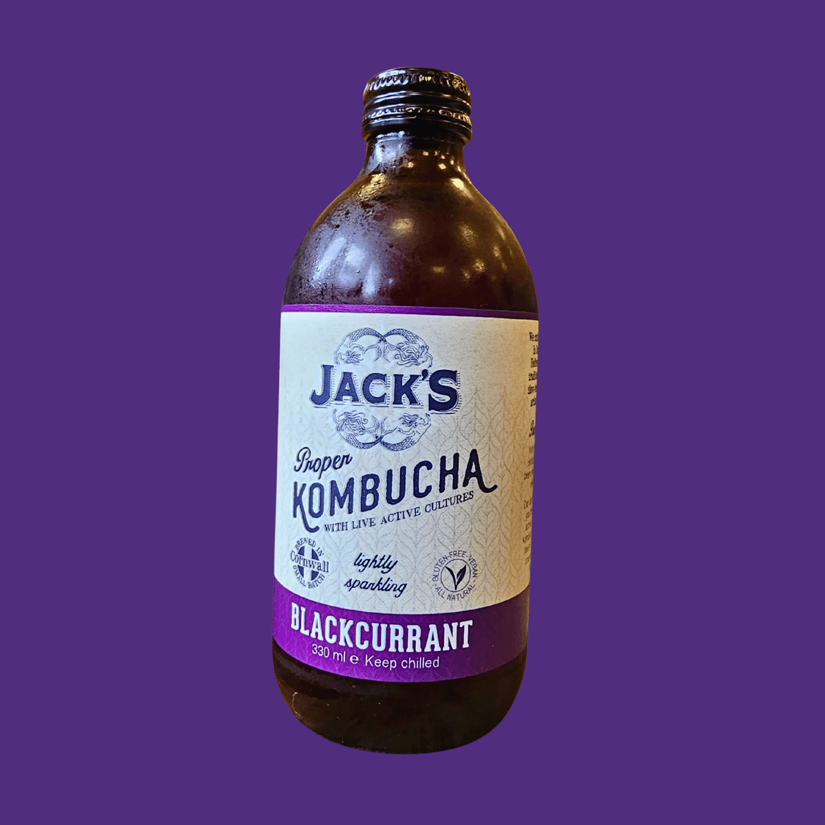 A bottle of Jack's Blackcurrant raw kombucha on a deep purple background.