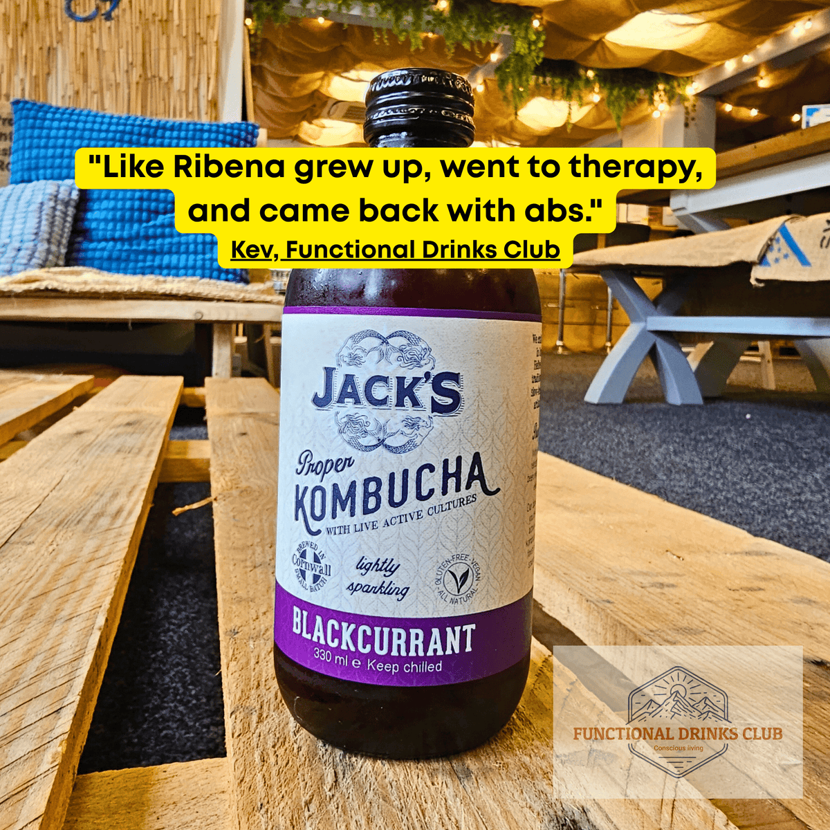 Jack's Blackcurrant raw kombucha on a wooden pallet table in the Otley taproom, with Kev's tasting note: "Like Ribena grew up, went to therapy, and came back with abs."