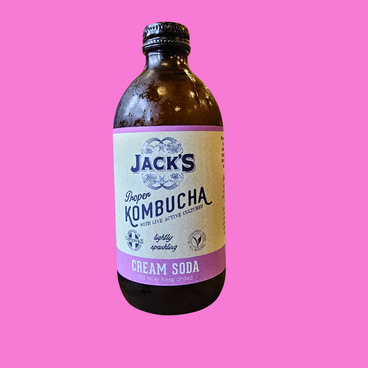 A bottle of Jack's Cream Soda raw kombucha on a bright pink background.