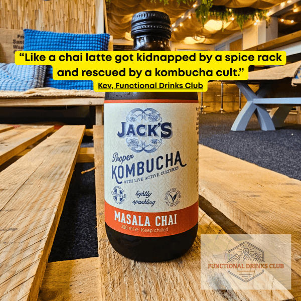 Jack's Masala Chai raw kombucha on a wooden pallet table in the Otley taproom, with Kev's tasting note: "Like a chai latte got kidnapped by a spice rack and rescued by a kombucha cult."
