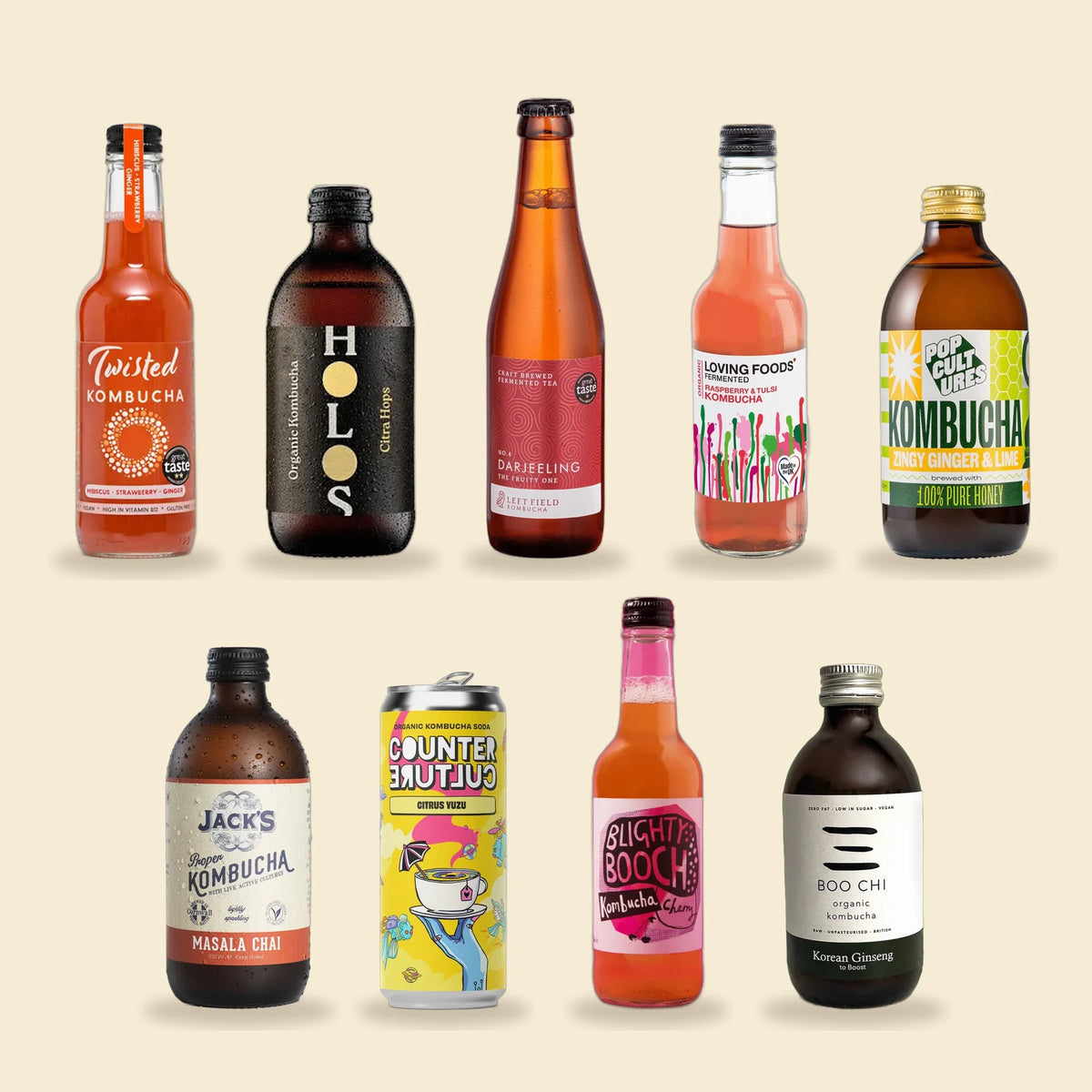 A pick-and-mix of raw kombucha from nine UK makers, including Twisted, HOLOS, Left Field, Loving Foods, Pop Cultures, Jack's, Counter Culture, Blighty Booch and Boo Chi, on a sand background.