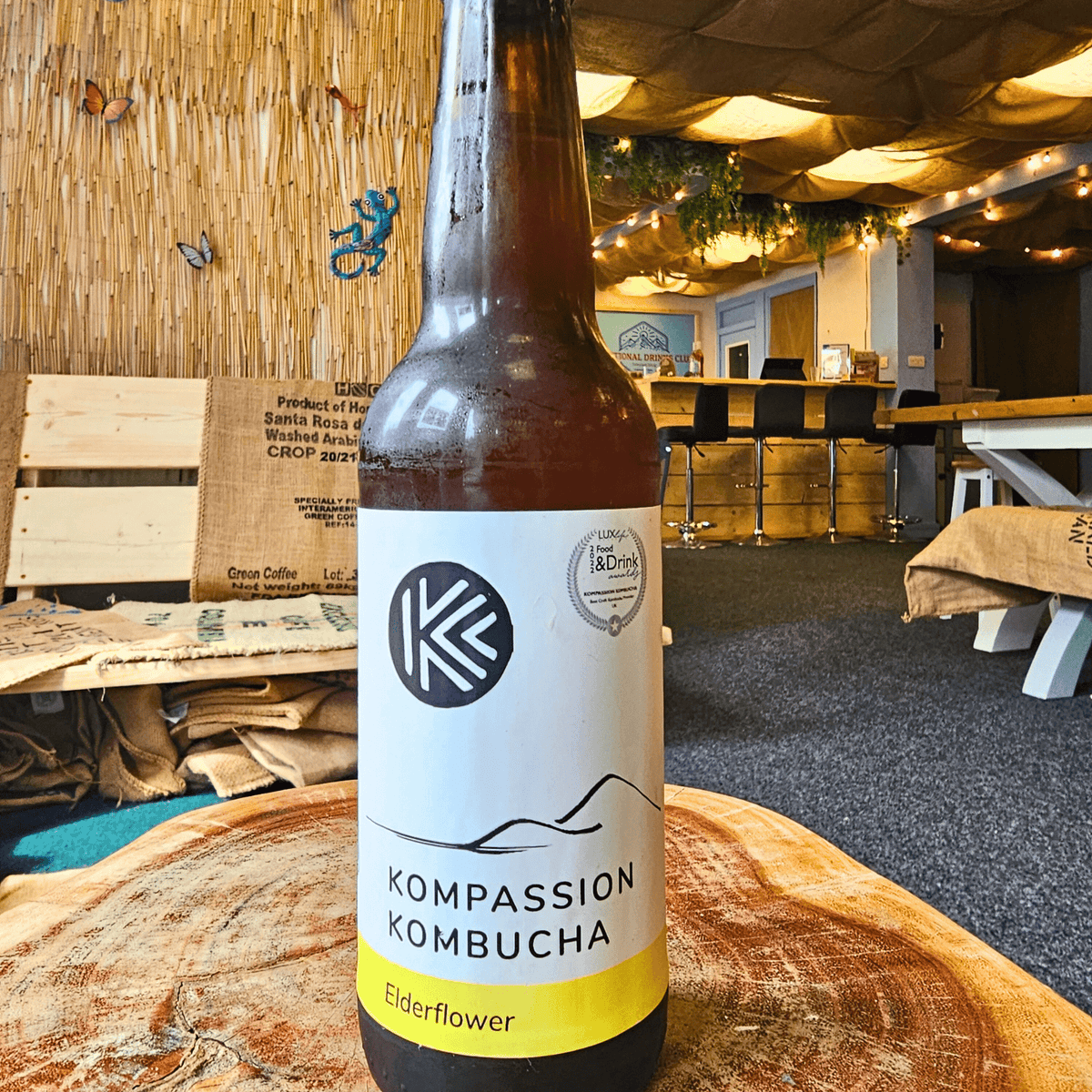 A bottle of Kompassion Elderflower raw kombucha on a tree-trunk table in the Otley taproom.
