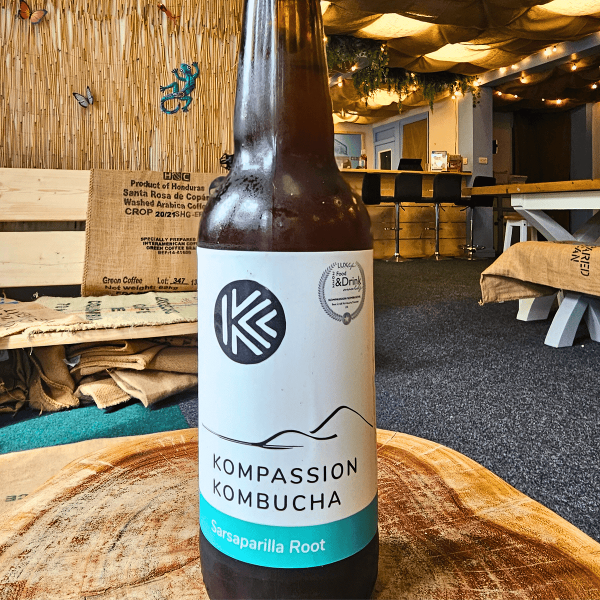 A bottle of Kompassion Sarsaparilla Root raw kombucha on a tree-trunk table in the Otley taproom.