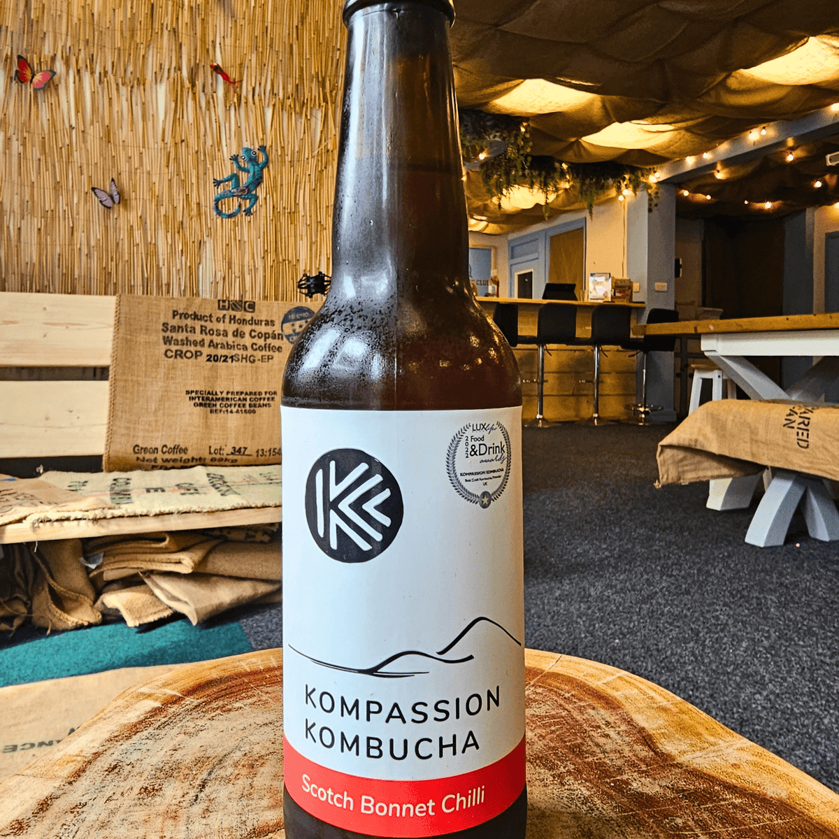 A bottle of Kompassion Scotch Bonnet Chilli raw kombucha on a tree-trunk table in the Otley taproom.