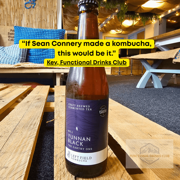 Left Field No.1 Yunnan Black raw kombucha on a wooden pallet table in the Otley taproom, with Kev's tasting note: "If Sean Connery made a kombucha, this would be it."