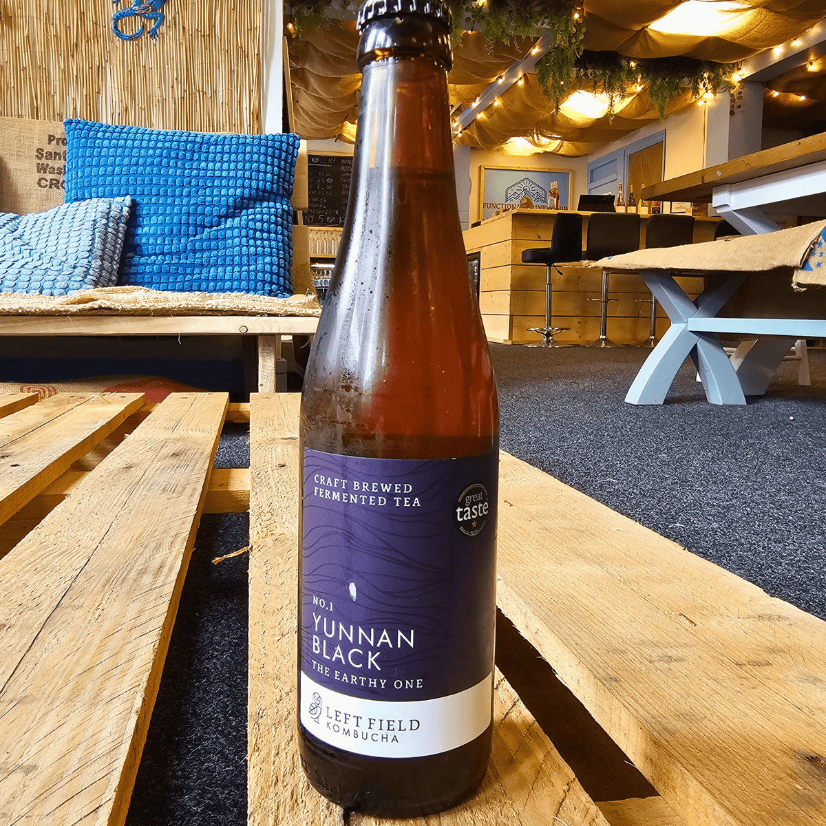 A bottle of Left Field No.1 Yunnan Black raw kombucha on a wooden pallet table in the Otley taproom.