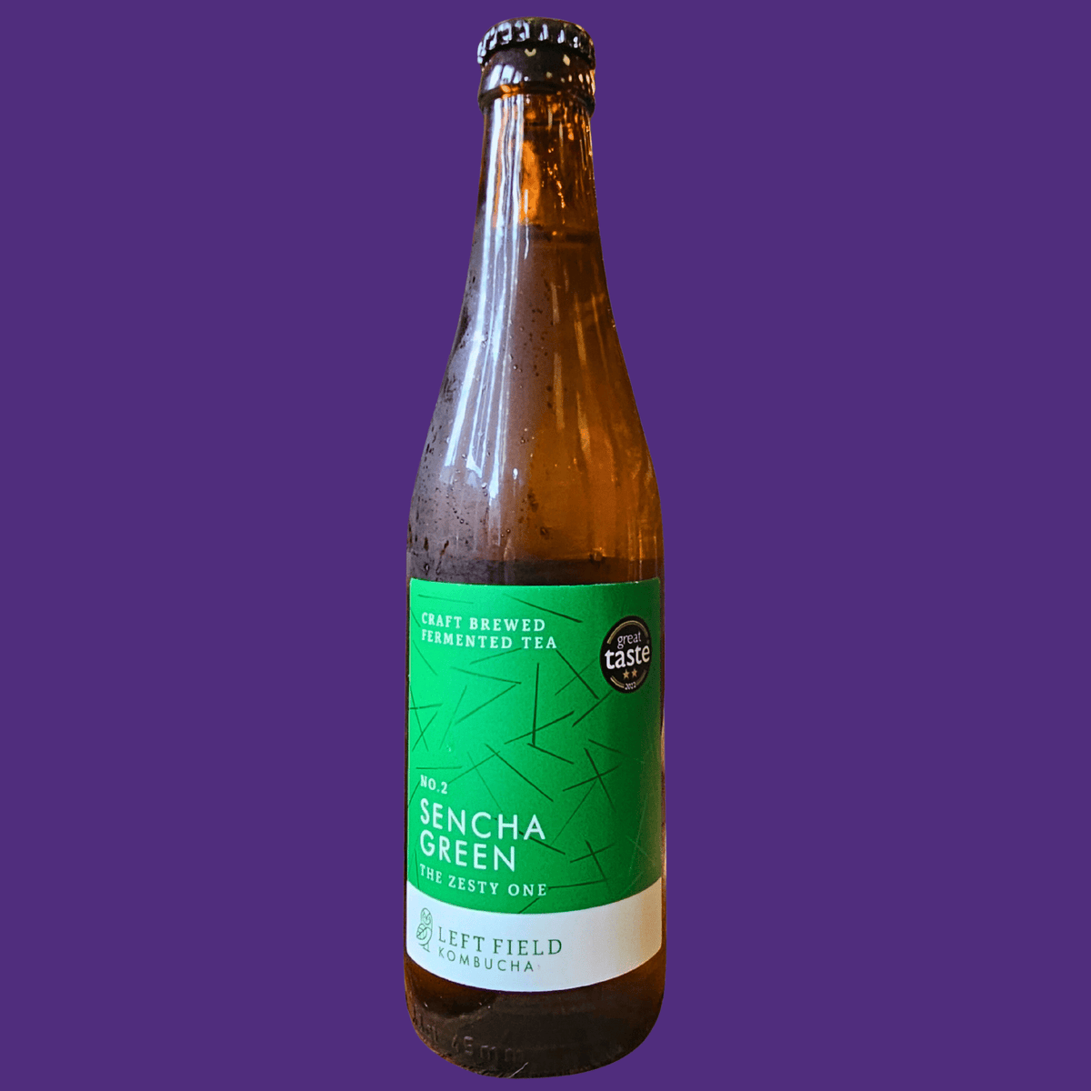 A bottle of Left Field No.2 Sencha Green raw kombucha on a deep purple background.