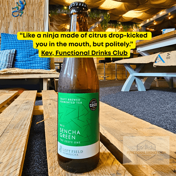 Left Field No.2 Sencha Green raw kombucha on a wooden pallet table in the Otley taproom, with Kev's tasting note: "Like a ninja made of citrus drop-kicked you in the mouth, but politely."