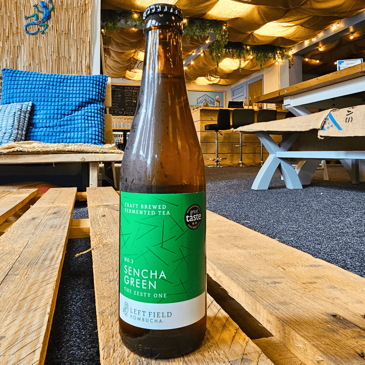 A bottle of Left Field No.2 Sencha Green raw kombucha on a wooden pallet table in the Otley taproom.