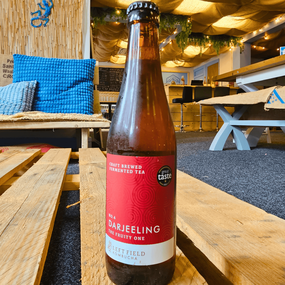 A bottle of Left Field No.4 Darjeeling raw kombucha on a wooden pallet table in the Otley taproom.