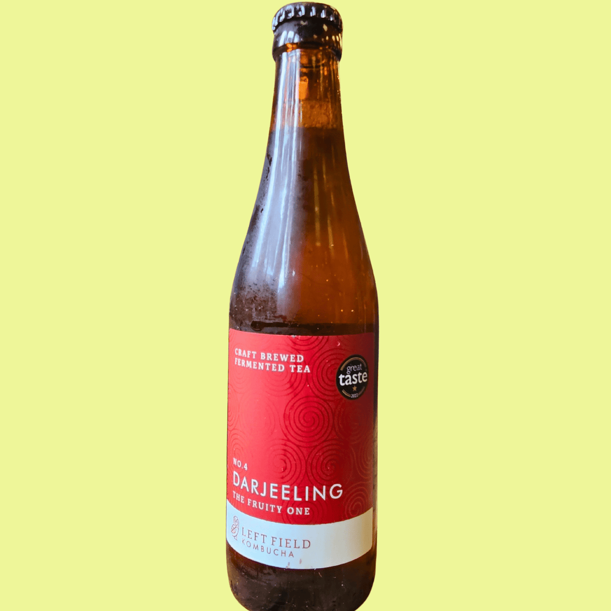 A bottle of Left Field No.4 Darjeeling raw kombucha on a pale yellow background.