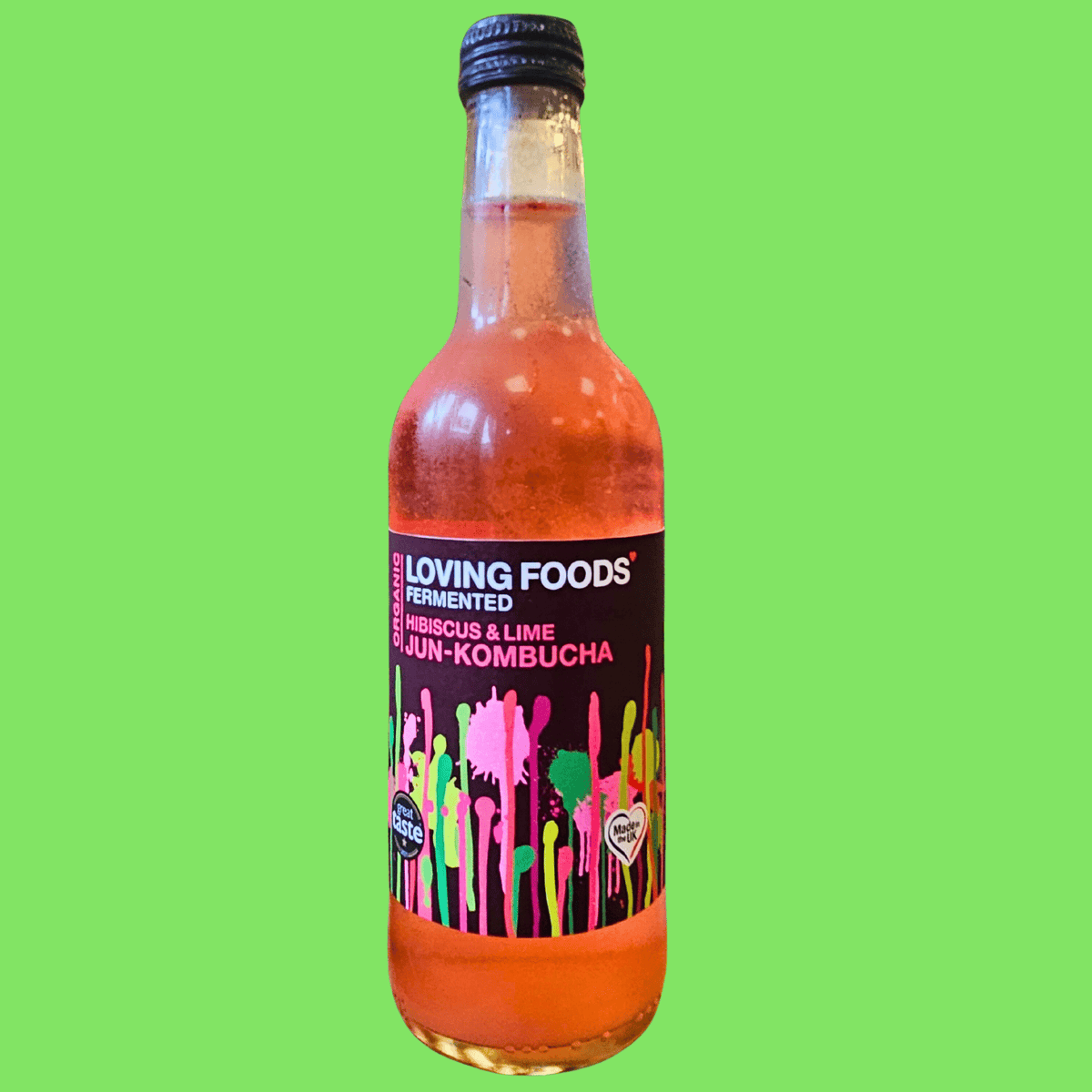 A bottle of Loving Foods Hibiscus & Lime raw jun kombucha on a bright green background.