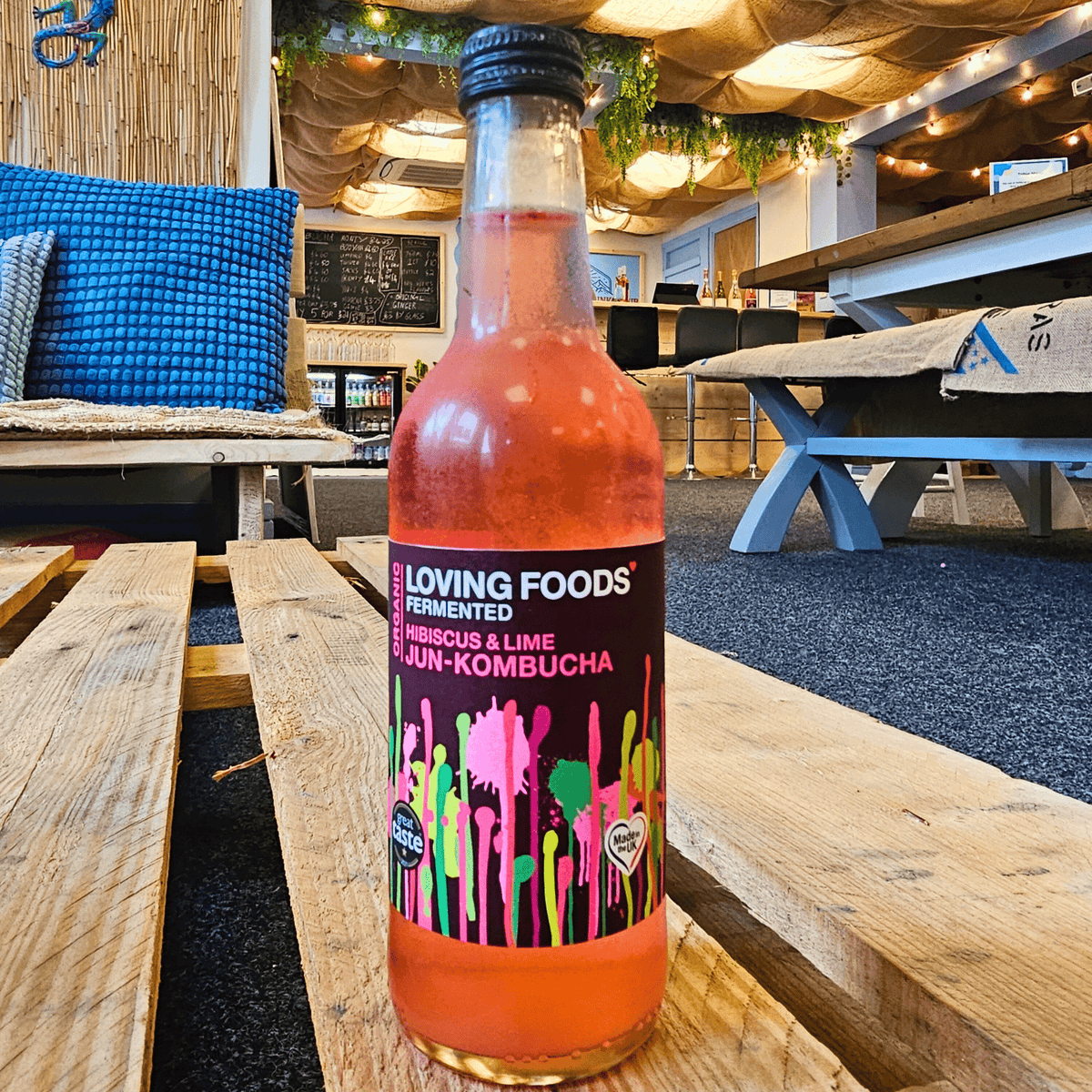 A bottle of Loving Foods Hibiscus & Lime raw jun kombucha on a wooden pallet table in the Otley taproom.