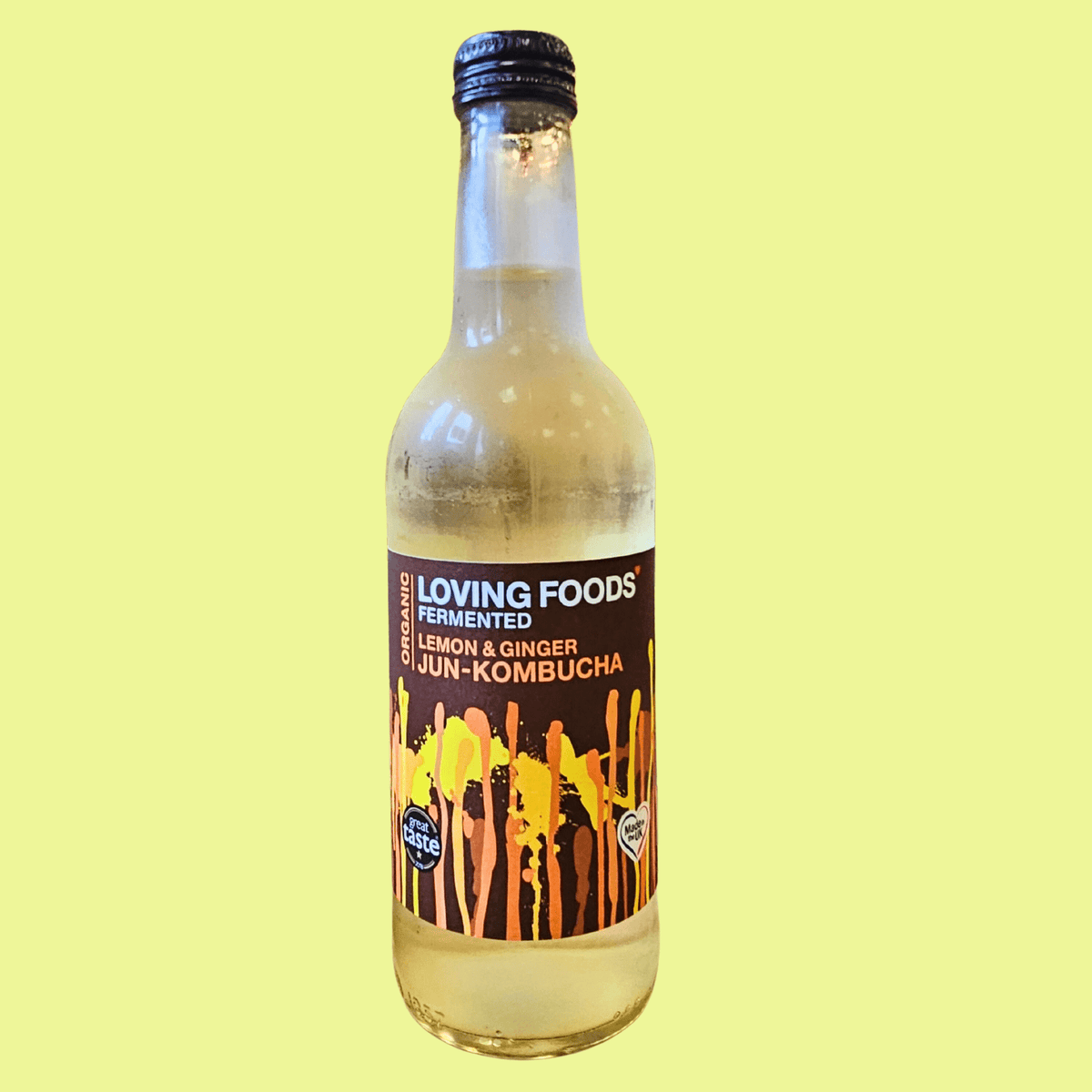 A bottle of Loving Foods Lemon & Ginger raw jun kombucha on a pale yellow background.