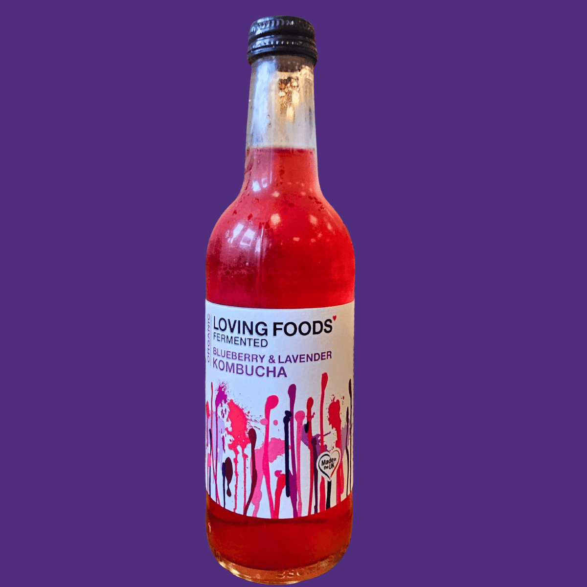 A bottle of Loving Foods Blueberry & Lavender raw kombucha on a deep purple background.