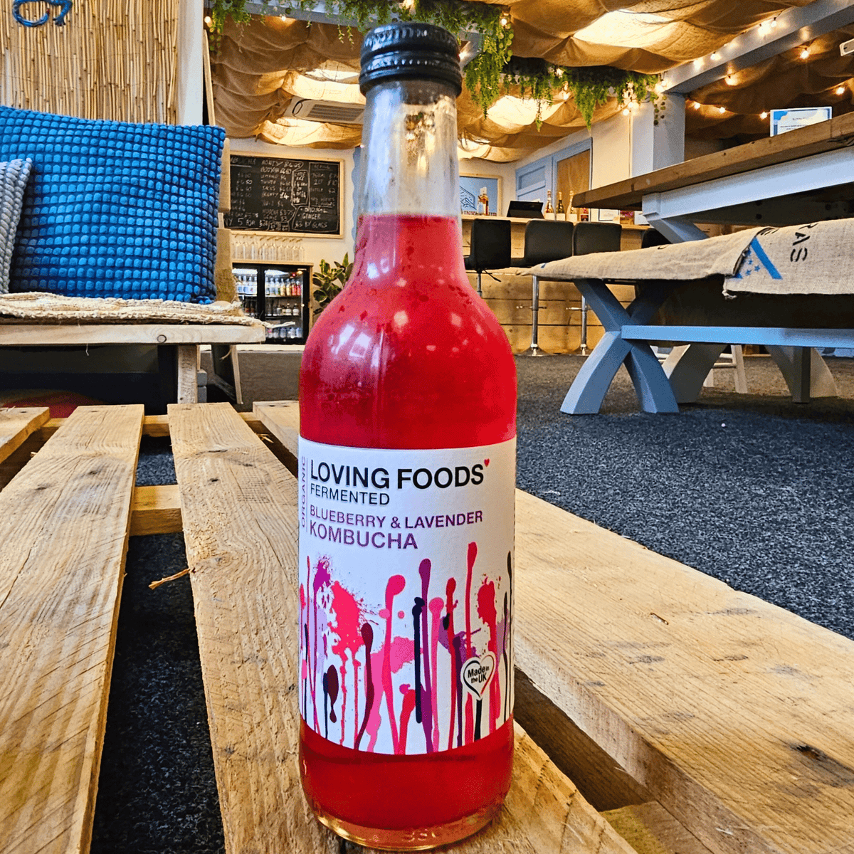 A bottle of Loving Foods Blueberry & Lavender raw kombucha on a wooden pallet table in the Otley taproom.