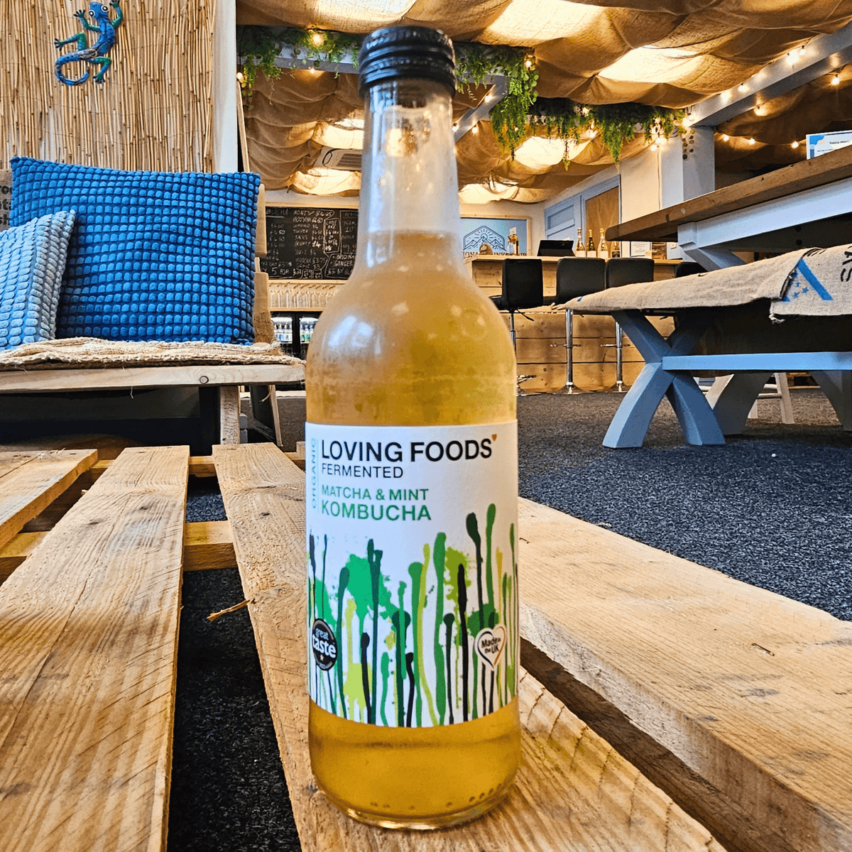 A bottle of Loving Foods Matcha & Mint raw kombucha on a wooden pallet table in the Otley taproom.