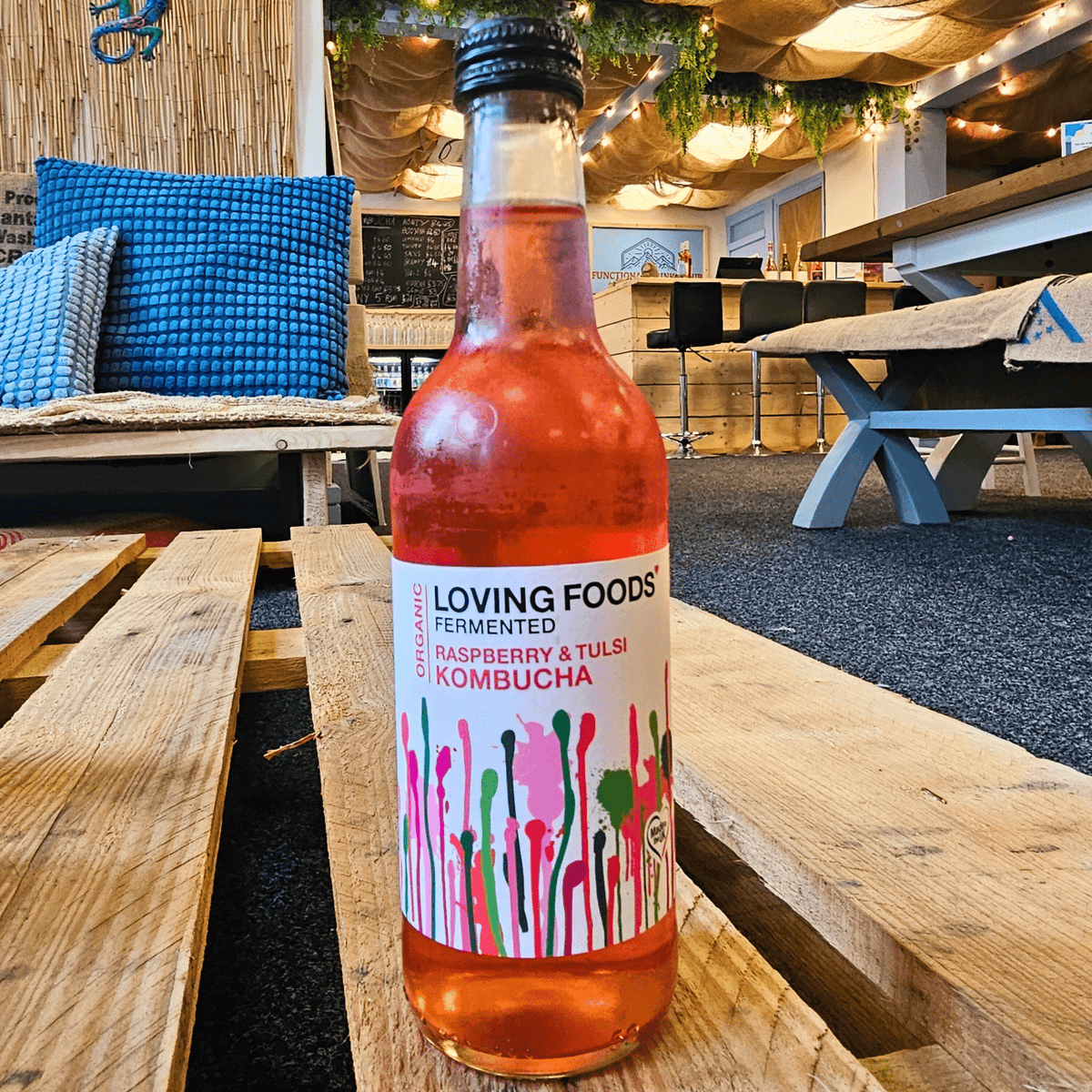 A bottle of Loving Foods Raspberry & Tulsi raw kombucha on a wooden pallet table in the Otley taproom.