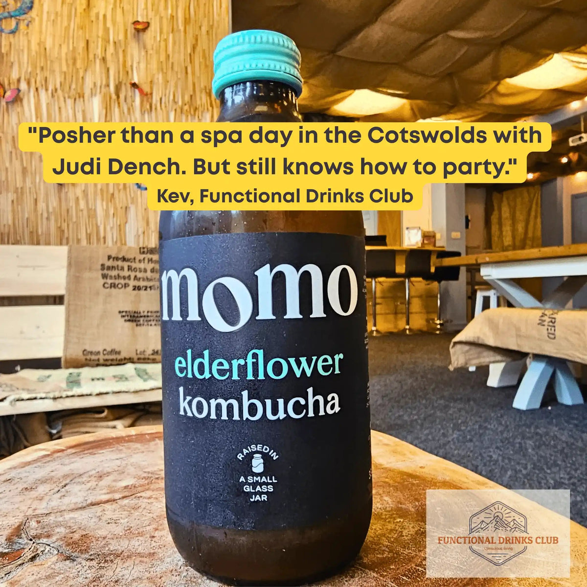 MOMO Elderflower raw kombucha on a tree-trunk table in the Otley taproom, with Kev's tasting note: "Posher than a spa day in the Cotswolds with Judi Dench. But still knows how to party."