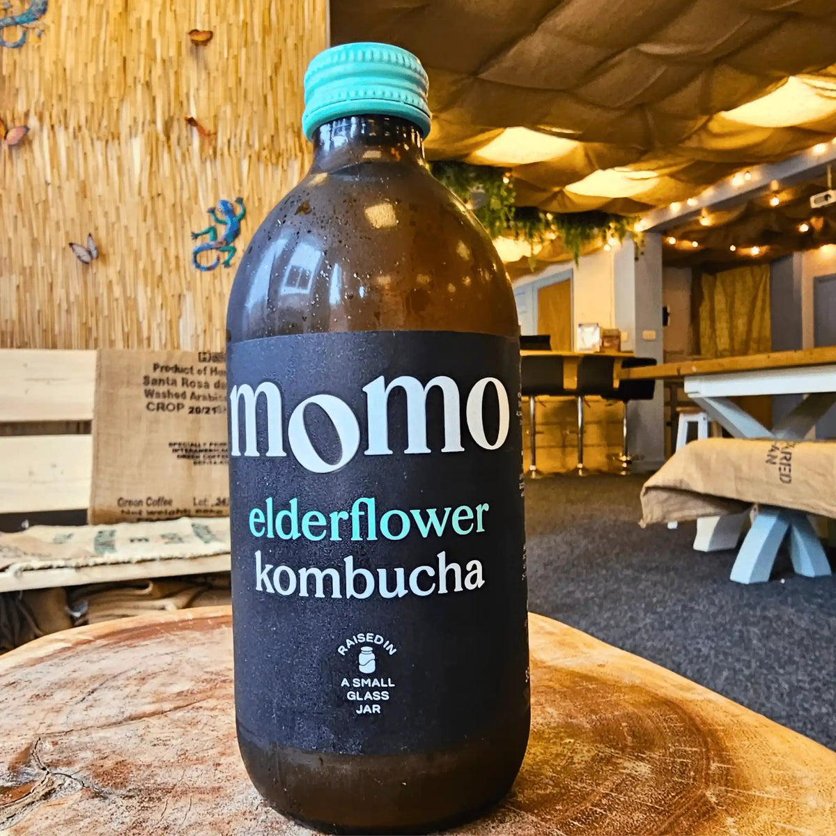 A bottle of MOMO Elderflower raw kombucha on a tree-trunk table in the Otley taproom.