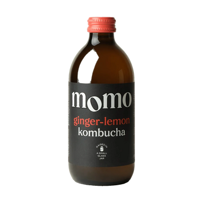 MOMO Ginger & Lemon raw kombucha in an amber glass bottle with a coral cap and a black label with coral lettering.