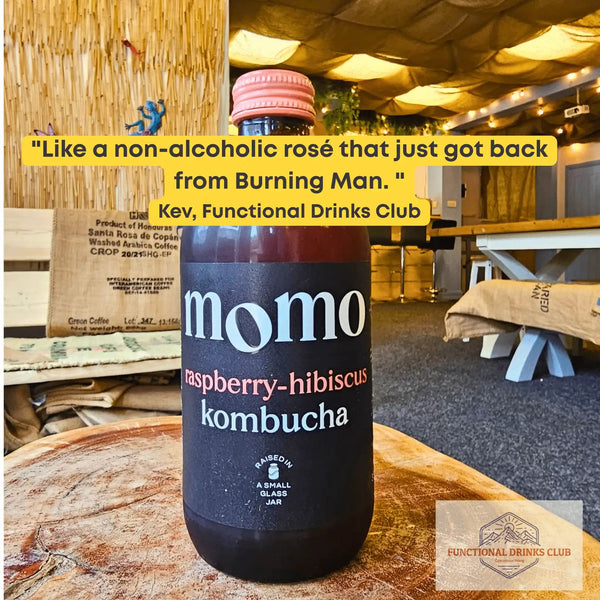 MOMO Raspberry & Hibiscus raw kombucha on a tree-trunk table in the Otley taproom, with Kev's tasting note: "Like a non-alcoholic rosé that just got back from Burning Man."