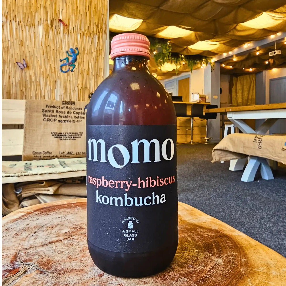 A bottle of MOMO Raspberry & Hibiscus raw kombucha on a tree-trunk table in the Otley taproom.