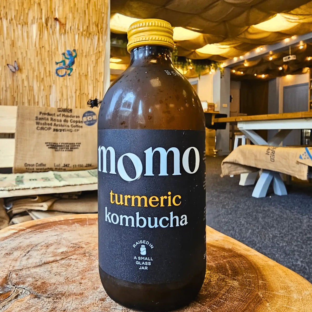 A bottle of MOMO Turmeric raw kombucha on a tree-trunk table in the Otley taproom.