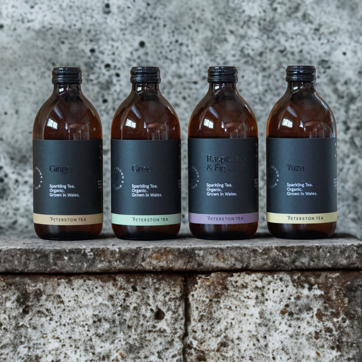 Peterston Tea kombucha in Ginger, Green, Raspberry & Fig and Yuzu lined up on a stone ledge.