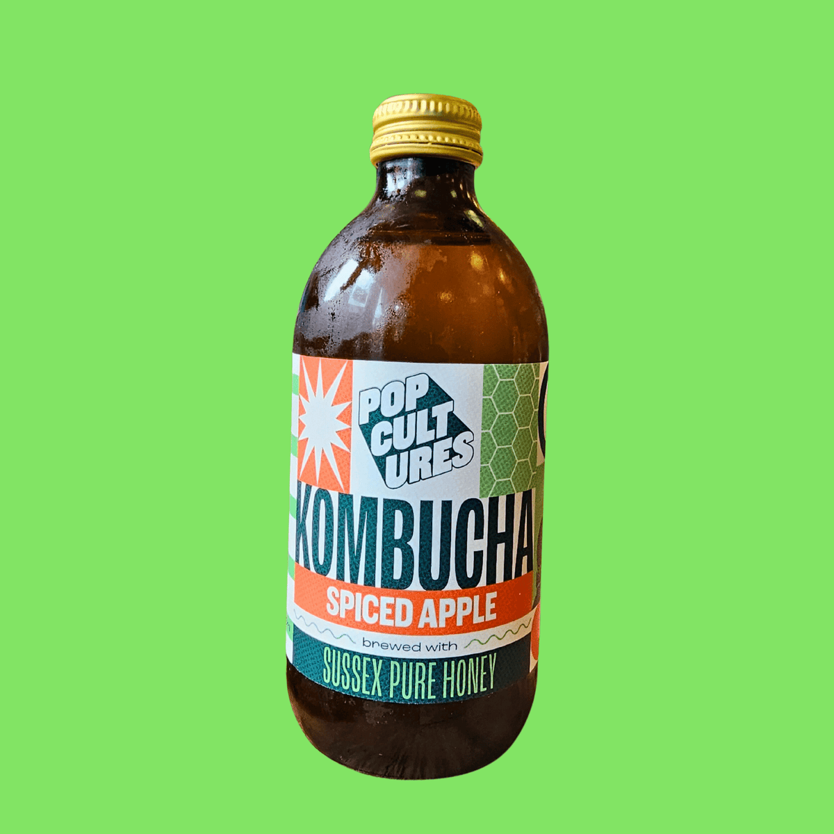 A bottle of Pop Cultures Apple & Cardamom raw jun kombucha on a bright green background.